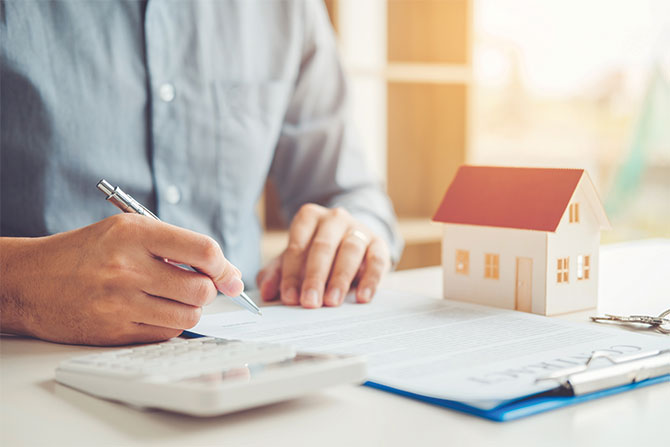 man-with-pen-and-paper-and-little-cardboard-house-on-desk