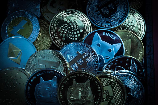 Community Banks and Crypto-Assets; A collection of various cryptocurrency coins, including Bitcoin, Ethereum, and Shiba Inu, with a metallic sheen and a dark, moody tone.