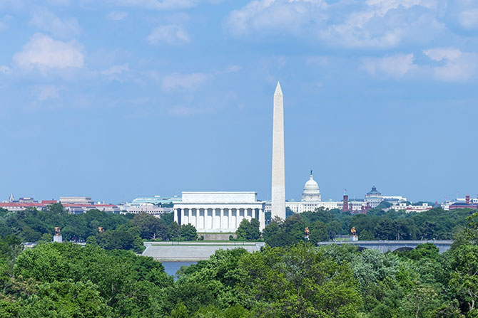 Washington Update: Fighting on in 2026; View of Washington, D.C. skyline featuring the Washington Monument, Lincoln Memorial, and U.S. Capitol under a blue sky, surrounded by lush green trees.