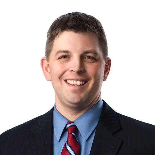 Randall Saunders; Smiling man in a dark pinstripe suit, blue shirt, and red striped tie against a plain white background, conveying professionalism and friendliness.